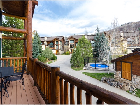 A peaceful mountain community setting featuring nearby homes, landscaped grounds, and a shared pool area surrounded by alpine slopes and evergreen trees.