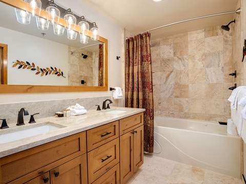 Your private bathroom features a spacious tub-shower combo with elegant stone tile, dual sinks with ample counter space, and plush towels waiting for you to unwind after a day of adventure.