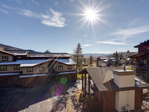 Bright winter sunlight illuminates the surrounding mountain resort area, with snow-dusted rooftops and distant valley views framing this peaceful neighborhood setting.