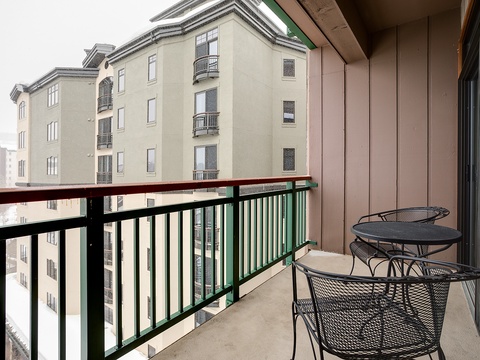 Private balcony with cozy seating overlooking neighboring residential buildings in a peaceful mountain setting.