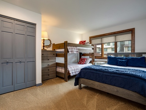 Rest easy in this thoughtfully designed bedroom featuring a plush queen bed and cozy bunk beds. Natural light streams through the window while ample storage keeps your belongings organized.