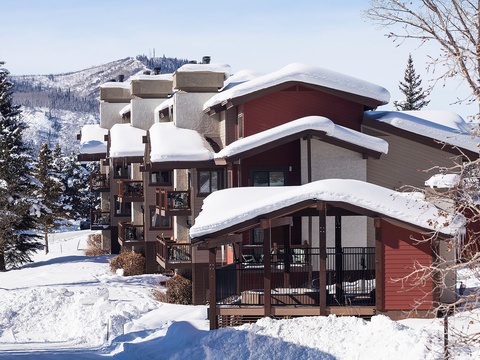 A picturesque winter retreat nestled in snowy mountain terrain, featuring inviting architecture and panoramic views of pristine slopes and forested peaks.