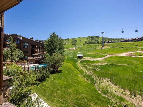Mountain resort property situated beside ski slopes with gondola access, featuring an outdoor pool area surrounded by mature trees and expansive lawn, offering direct access to year-round alpine recreation.