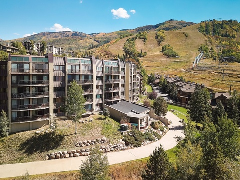 Multi-level property nestled at the base of mountain slopes, surrounded by landscaped grounds and alpine scenery, offering convenient access to outdoor recreation.