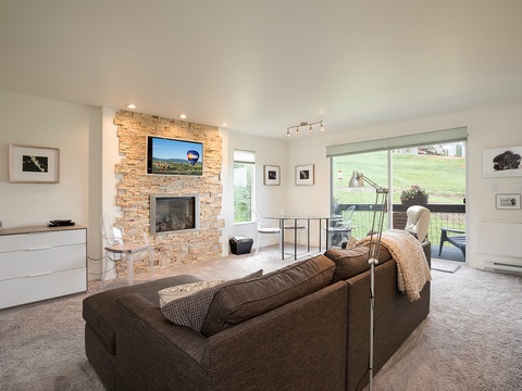 Unwind in your bright living room with cozy seating, a warm stone fireplace, and sliding doors that open to peaceful countryside views—perfect for relaxing after exploring nearby.
