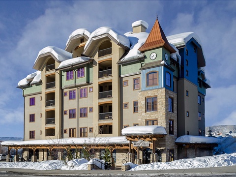 Charming alpine-inspired building nestled in a snowy mountain setting, featuring distinctive architecture with a clock tower and colorful accents.