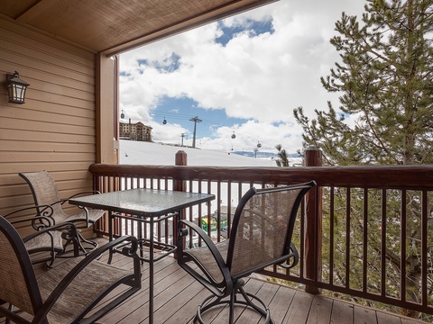 A covered mountain-view balcony offers ski slope views and relaxing dining space under blue skies framed by evergreens.