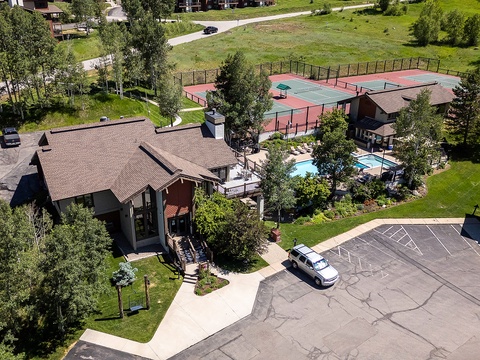 Aerial view of the property showing the main building, swimming pool area, tennis courts, and ample parking surrounded by mature trees and green lawns.