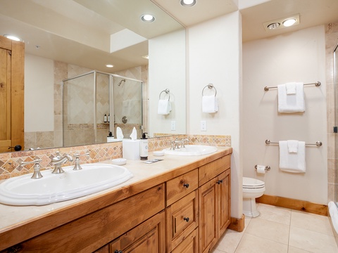 Your spacious bathroom features dual vanities with elegant tile countertops, a refreshing walk-in shower, and warm wood cabinetry—perfect for getting ready each morning in comfort.