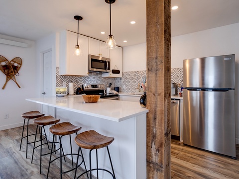 Your open kitchen features modern stainless appliances, sleek white counters, and a charming breakfast bar where you can sip morning coffee beneath warm pendant lights.