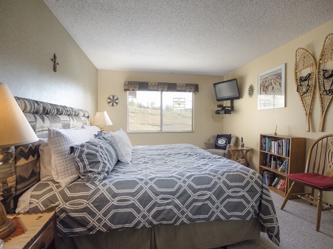 Cozy mountain-inspired bedroom with vintage snowshoes, geometric bedding, and scenic window views. Curl up with a good book from the mini library and unwind after your adventures.