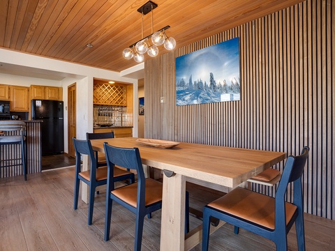 Gather around this handsome wood table beneath a warm plank ceiling and modern pendant lighting—your mountain retreat awaits, with a cozy kitchen just steps away for easy entertaining.