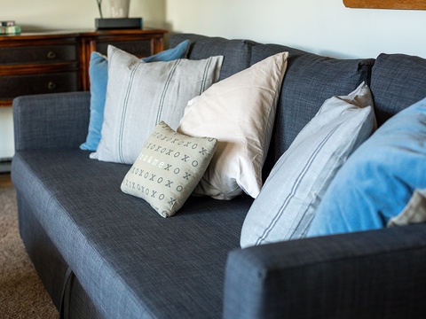 Sink into the plush charcoal sofa piled with soft pillows in calming blues and creams—your perfect spot to unwind with a book or morning coffee.