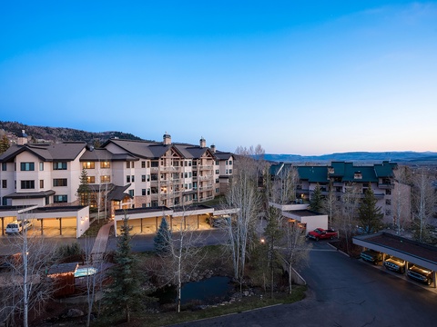 A mountain resort community nestled in the valley, featuring multi-level accommodations with covered parking, surrounded by evergreens and framed by distant peaks under an open sky.