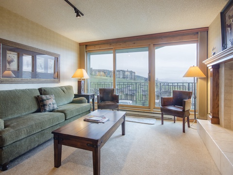 Unwind on the cozy sofa by the fireplace while enjoying stunning mountain views through your private balcony doors—your perfect retreat for relaxation and comfort.