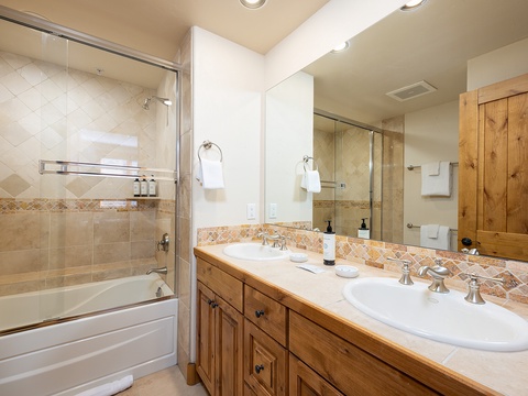 Your private bathroom features dual sinks with rustic wood cabinetry, warm tile accents, and a spacious tub-shower combo—perfect for refreshing after a day of mountain adventures.