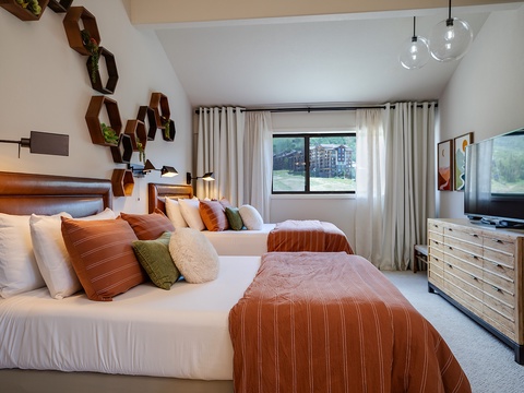 Sink into plush bedding with soft linens and decorative pillows, surrounded by warm wood accents and modern touches. Your private retreat features stylish hexagonal wall décor, thoughtful lighting, and a flat-screen TV for cozy evenings.