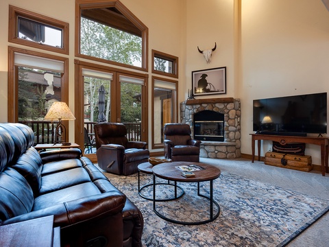Relax in your spacious living room with vaulted ceilings, a cozy stone fireplace, and plush leather seating. Floor-to-ceiling windows frame tranquil forest views, creating a warm mountain escape.