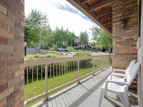 A peaceful property nestled in a quiet, tree-lined neighborhood provides a serene arrival and private covered balcony with two chairs overlooking the tranquil surroundings.
