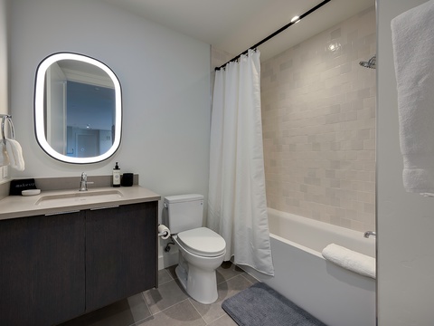Your modern bathroom features a sleek vanity, bright backlit mirror, and a spacious tub-shower combo for a relaxing start or end to your day.