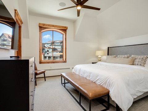 Unwind in this serene bedroom featuring a plush king bed, warm wood accents, and mountain views framed by an arched window. Relax under the gentle ceiling fan after your alpine adventures.