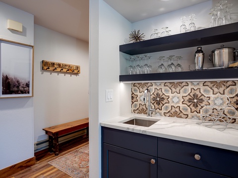 Your stylish wet bar features eye-catching patterned tile, sleek navy cabinetry, and open shelving stocked with glassware—perfect for crafting evening cocktails after exploring the area.