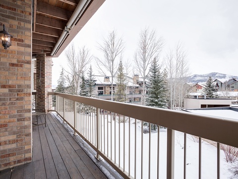 A spacious deck frames a picturesque winter scene with snow-covered evergreens, bare trees, and distant mountain peaks—perfect for taking in crisp mountain air during your stay.