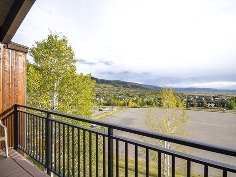 The property sits in a quiet neighborhood with views of surrounding mountains, residential areas, and open landscapes framed by aspen trees and green spaces visible from the balcony.