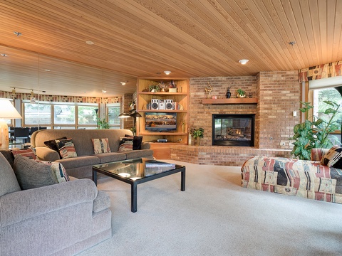 Settle into plush seating by the glowing fireplace, surrounded by warm wood ceilings and abundant natural light—your perfect space to unwind and feel right at home.