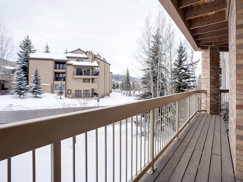 Private balcony overlooking a peaceful winter neighborhood with snow-dusted evergreens and distant mountain views, offering a serene outdoor retreat.