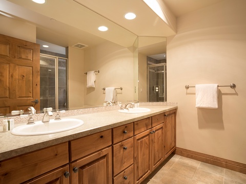 Step into your spacious dual-sink bathroom with warm wood cabinetry, elegant tile accents, soft lighting, and a walk-in shower awaiting your morning refresh or evening unwind.