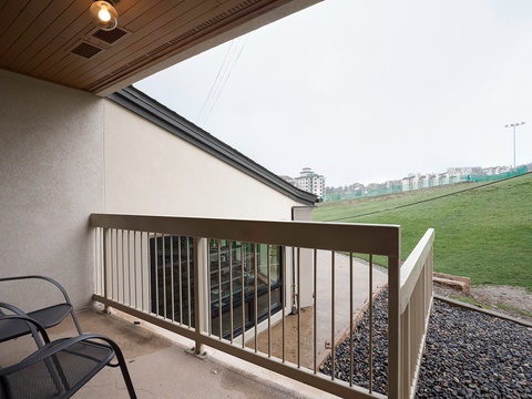 A covered terrace overlooks a landscaped slope with residential buildings beyond, providing a sheltered outdoor area at the property.