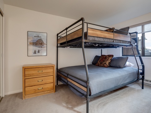 Your comfortable bunk room features a full-size bed below and twin above, with natural light streaming through large windows and a dresser for your belongings.