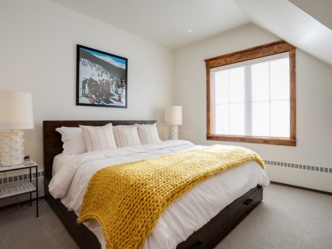 Sink into crisp white linens and a cozy yellow throw after your mountain adventures. Natural light streams through rustic wood framing, creating your perfect retreat.
