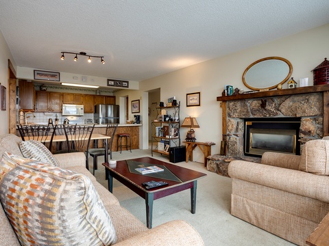 Relax in your spacious open-concept living area featuring a cozy stone fireplace, comfortable seating, and a fully-equipped kitchen ready for your mountain getaway meals.
