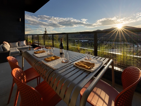 Enjoy golden hour from your private balcony, where mountains frame the horizon and an elegant outdoor dining setup awaits your evening meals under an expansive sky.