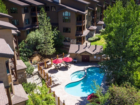 Aerial view of the resort property featuring an outdoor swimming pool surrounded by lush greenery, multi-story lodge buildings, and nearby recreational amenities.