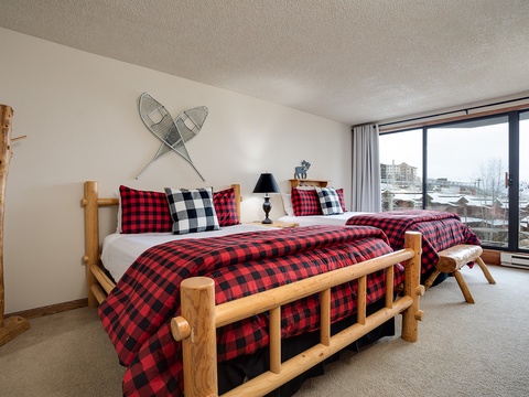 Cozy rustic charm meets comfort with handcrafted log beds dressed in plaid linens, while large windows reveal mountain vistas to inspire your alpine getaway.