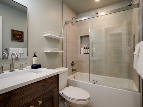 Your private bathroom features a sleek sliding glass shower, elegant white countertops, and soft, fluffy towels ready for your use.