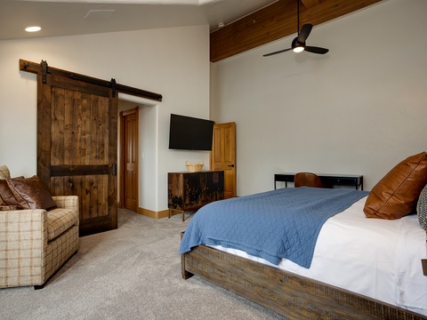Unwind in your spacious bedroom featuring rustic barn doors, a cozy sofa, and modern comforts like a flat-screen TV—your perfect retreat after a day of adventure.