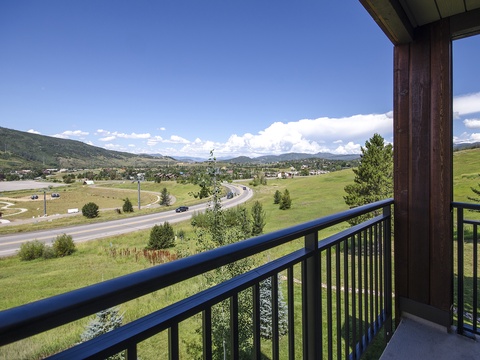 A scenic mountain valley panorama stretches across rolling green meadows and distant ridges under open blue skies, visible from the property's elevated position.