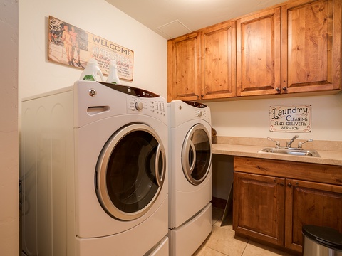 A dedicated laundry room with full-sized washer and dryer, warm wood cabinetry, and a utility sink makes keeping your wardrobe fresh effortless during your stay.