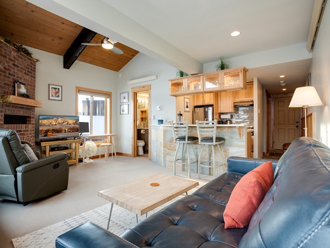 Step into your mountain retreat where warm wood tones meet cozy comfort. Sink into the leather sofa or recliner by the brick fireplace, while vaulted ceilings and natural light create an airy, inviting atmosphere throughout your open living space.