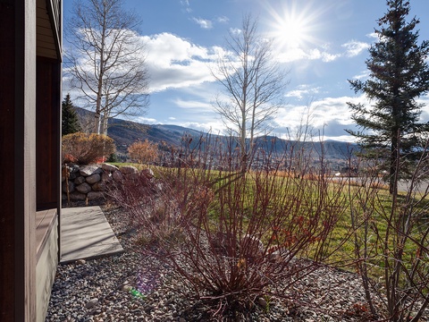 Stunning mountain views frame this vacation rental, with layers of dramatic peaks rising beyond open fields and bare deciduous trees in the foreground—a scenic mountain-side setting.