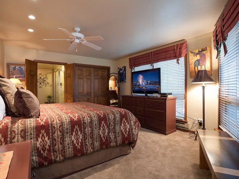 Your cozy mountain-style retreat features a plush bed with Southwest-inspired linens, a flat-screen TV, and custom wood furnishings. Natural light pours through large windows, inviting you to unwind in warmth and comfort.