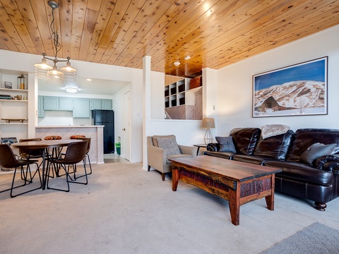 Unwind in your open living space beneath warm wood ceilings, where plush leather seating and a rustic coffee table invite you to relax after a day of mountain adventures.