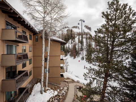 Ski-in/ski-out property nestled at the base of the slopes with direct mountain access, ski lift nearby, and seasonal winter snow blanketing the surrounding forested terrain.
