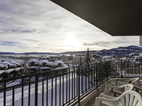 A winter mountain town nestled below snowy peaks unfolds beyond this elevated balcony, with nearby buildings and distant valleys creating a scenic backdrop for the property location.