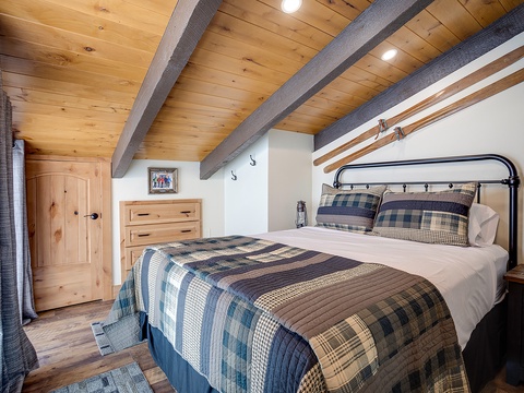 Unwind in your cozy loft bedroom with rustic wood beams, plaid quilted bedding, and warm pine finishes creating a charming retreat after a day of adventure.