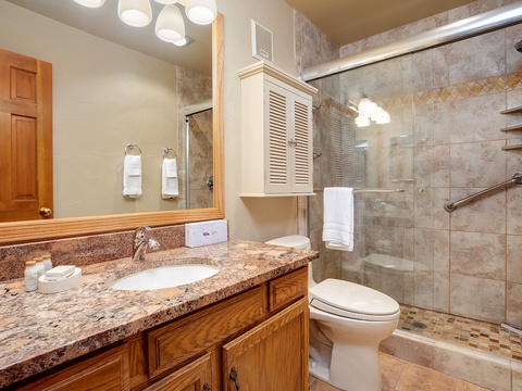 Step into your private bathroom with granite countertops, warm wood cabinetry, and a spacious walk-in shower with elegant tile details—your personal retreat awaits.